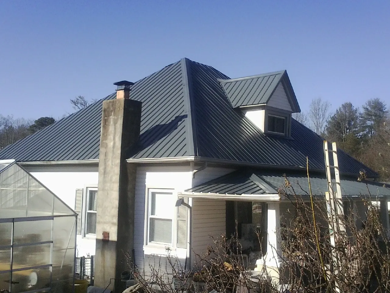 Dark blue standing seam metal roof on a white farmhouse with dormer — Slate & Tile Roof Repair by Roofing Brothers in Fiatt