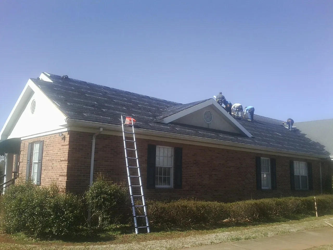 Crew tearing shingles off a brick ranch roof with a ladder set — Emergency Roof Repair work by our crew in Fiatt