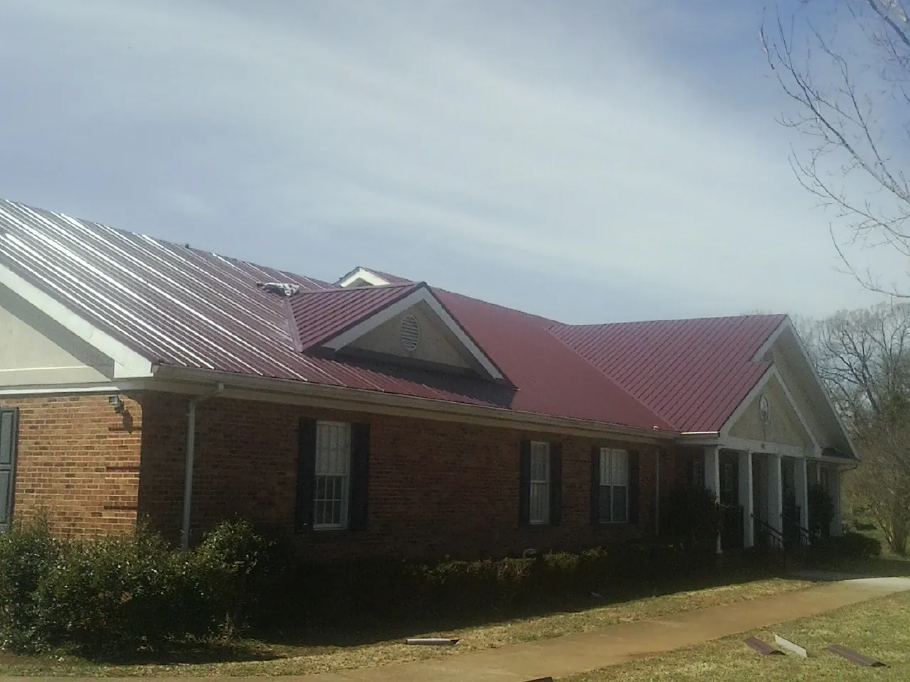 Red metal roof with gabled entries on a long brick building, from a Hail Damage Roof Repair job in Fiatt