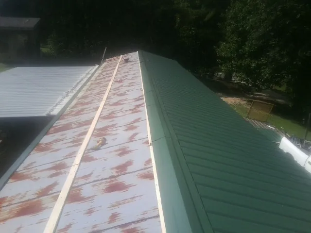 Old rusted panels beside newly installed green metal roofing — Wind Damage Roof Repair by Roofing Brothers in Fiatt