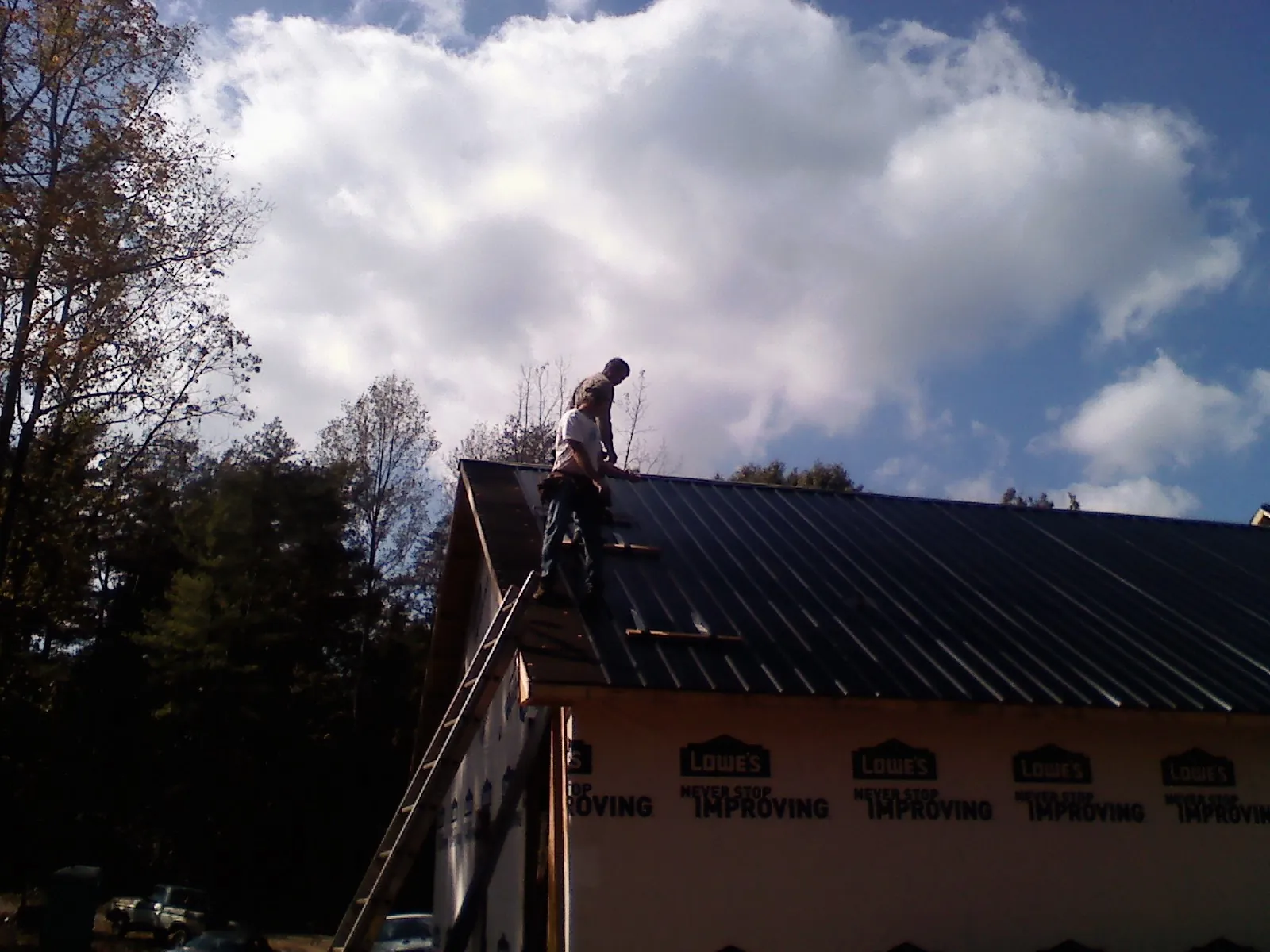 Roofer fastening dark metal panels high against a cloudy sky, from a Roof Inspection job in Fiatt